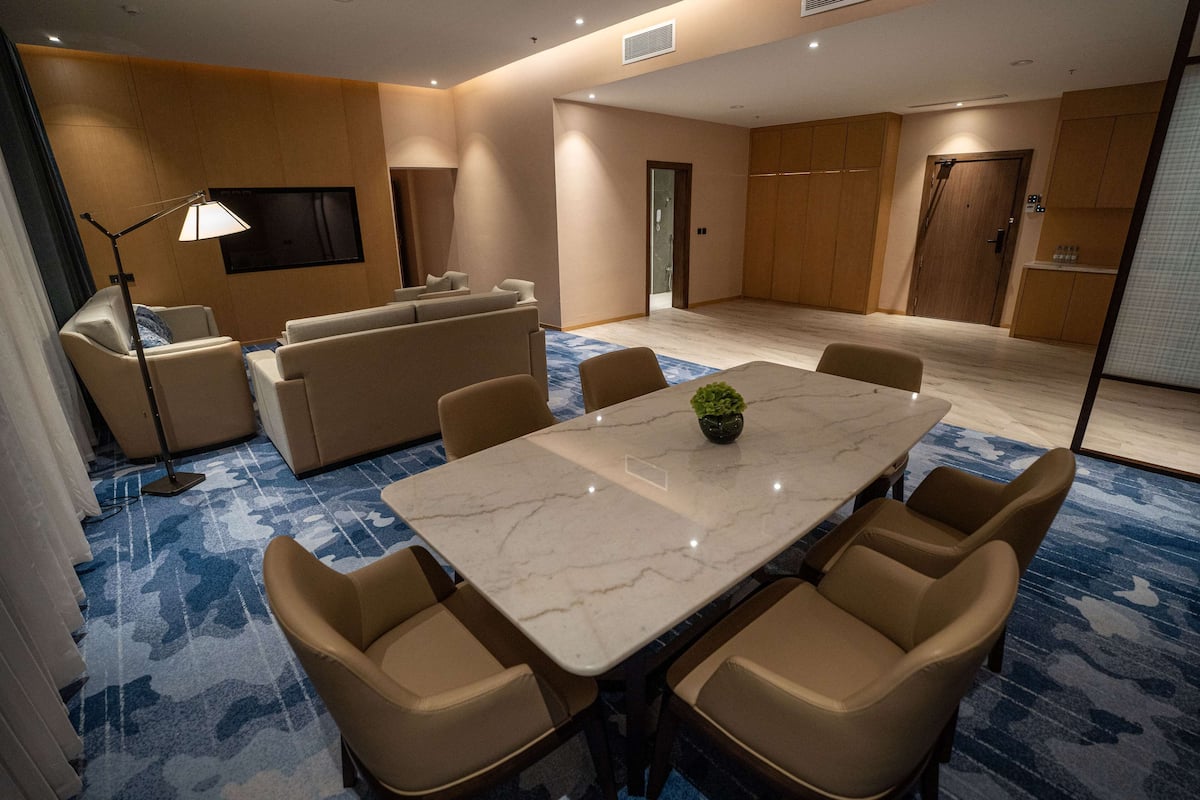 Una habitación de hotel moderna con una mesa de comedor de mármol, sofás color beige y una alfombra estampada azul.