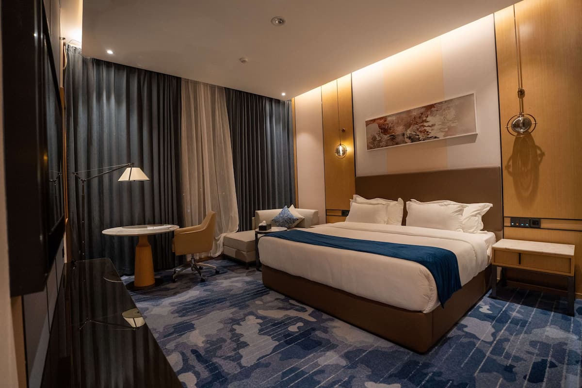 Una habitación de hotel con una cama grande, una mesita de noche, una silla, un escritorio y una lámpara.