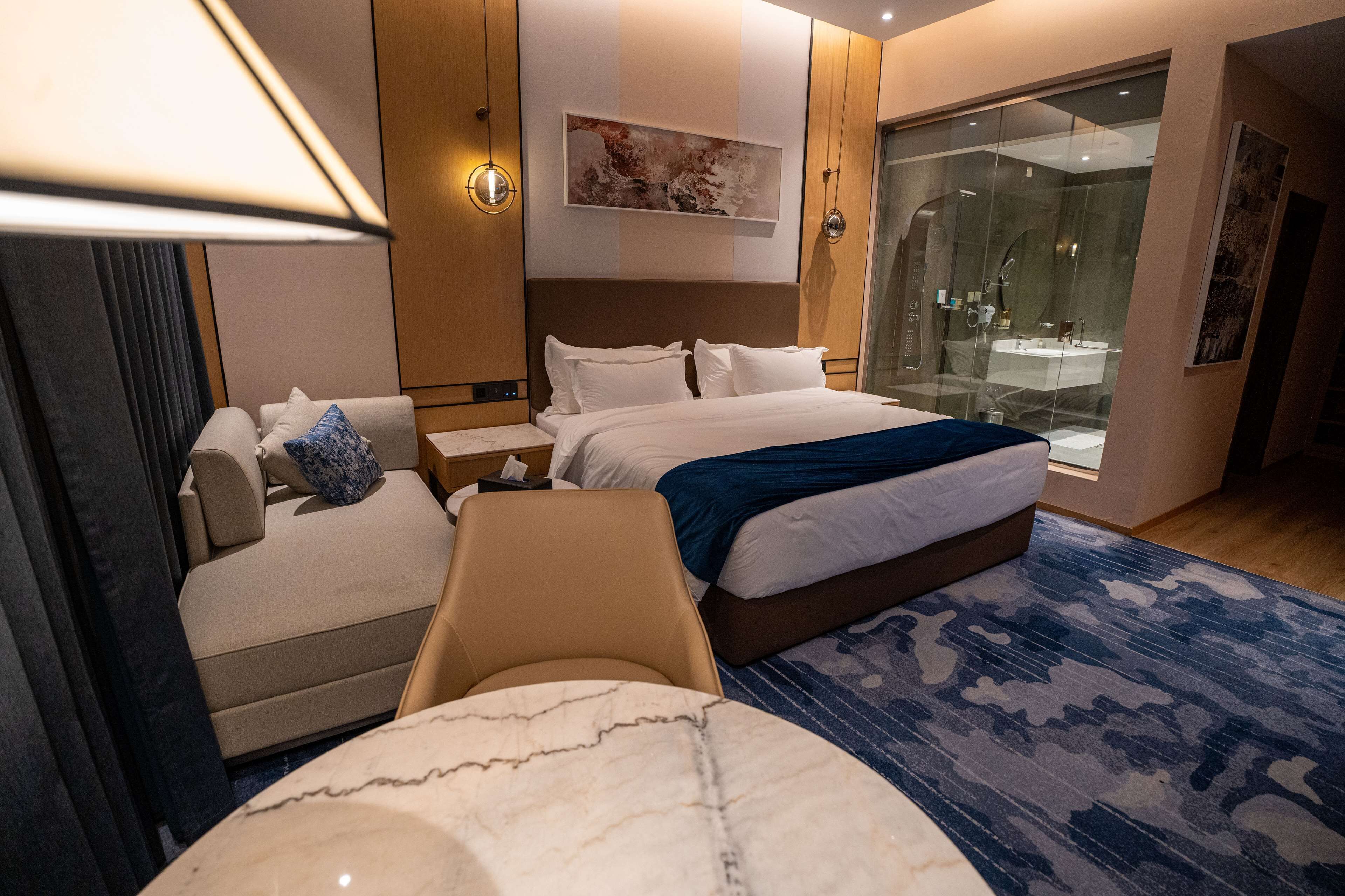 Camera d'albergo moderna con un ampio letto, una poltrona, una scrivania e un box doccia in vetro.