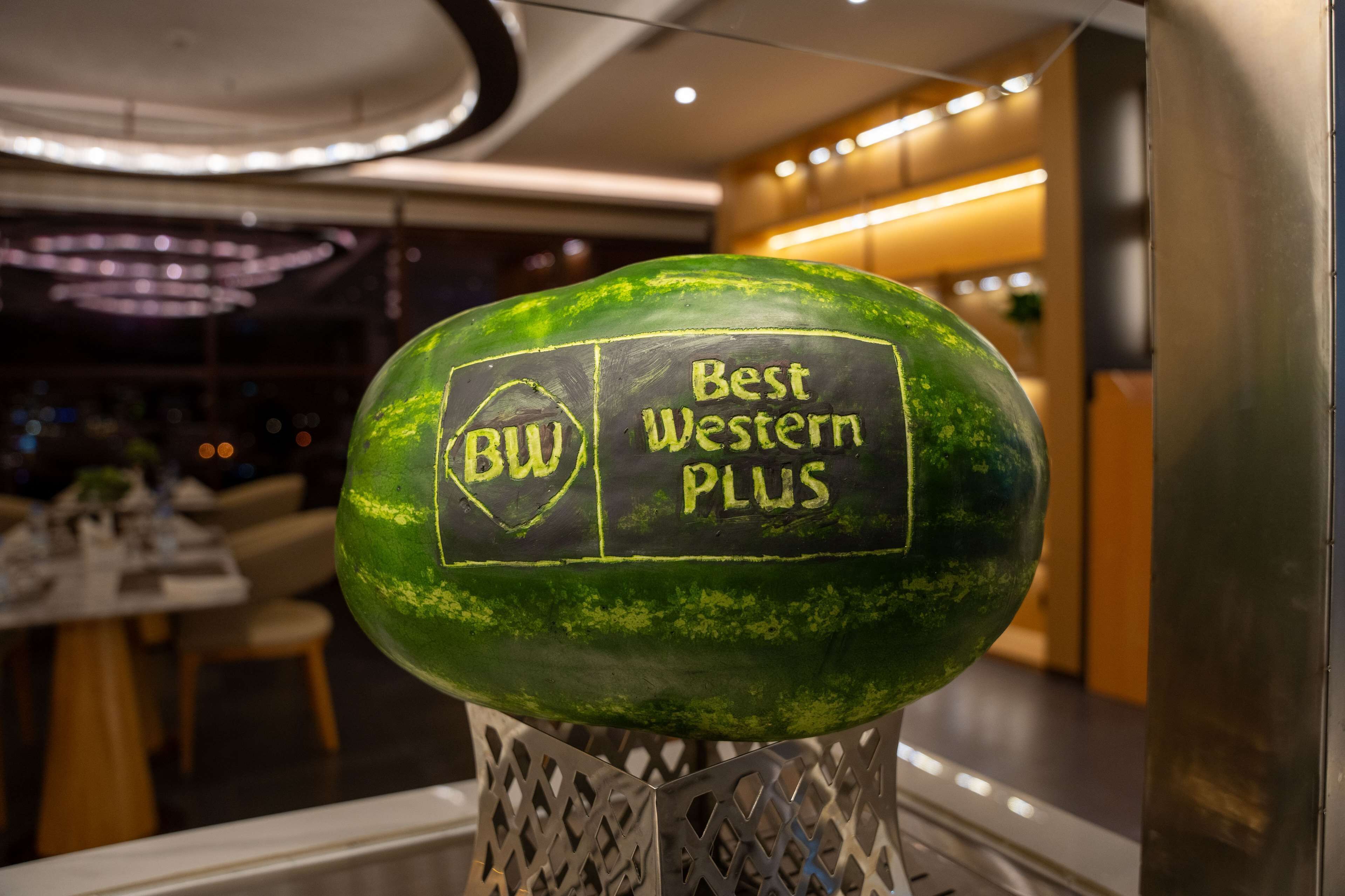 En vandmelon med teksten "BW Best Western PLUS" på, placeret på et dekorativt fad i en restaurant.
