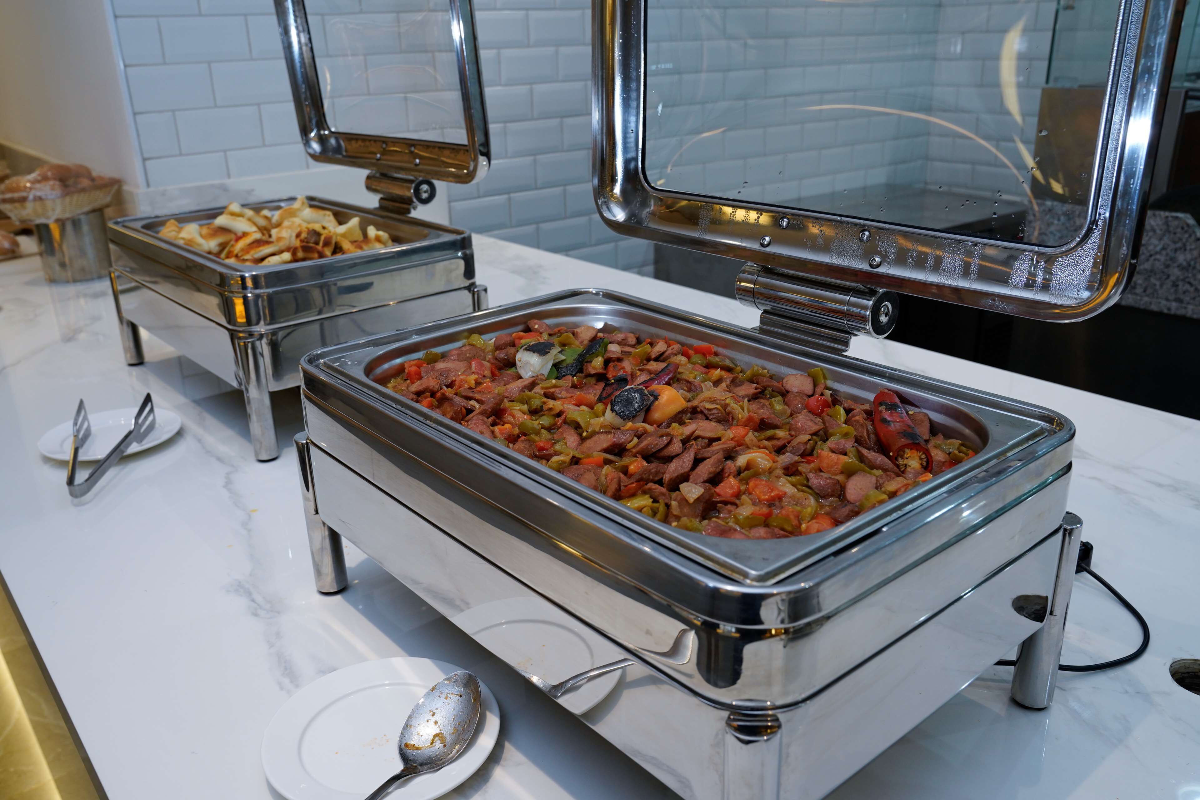 A buffet with various dishes, including a large container of mixed meats and vegetables, and a smaller container of pastries.