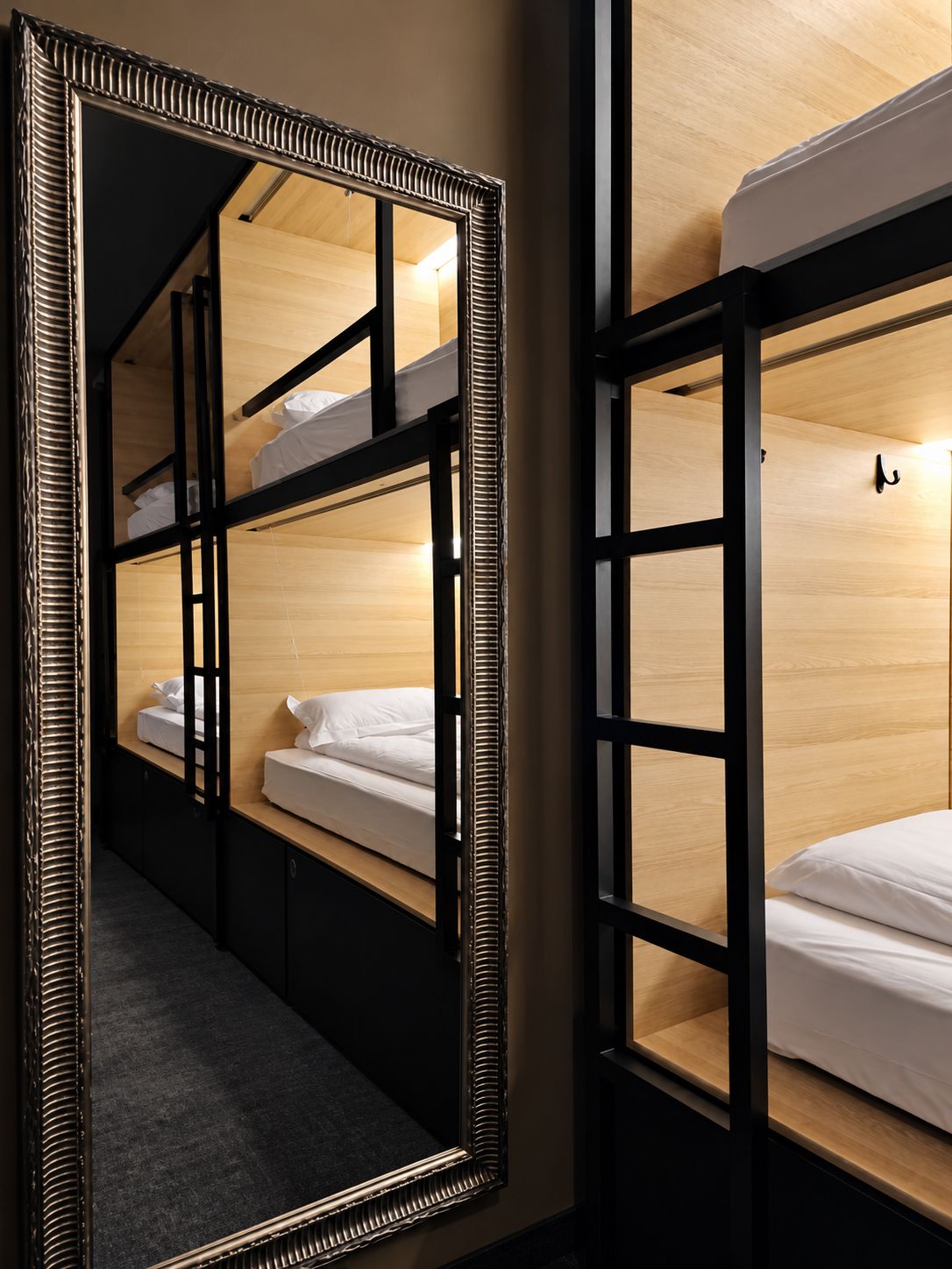 Habitación de hotel con literas, un espejo grande y una lámpara fijada a la pared.