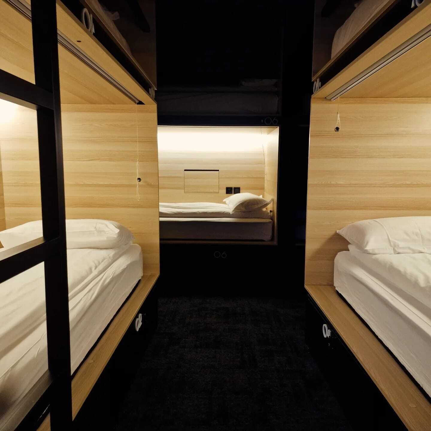 A narrow corridor leading to a room with two beds, wooden walls, and a carpeted floor.