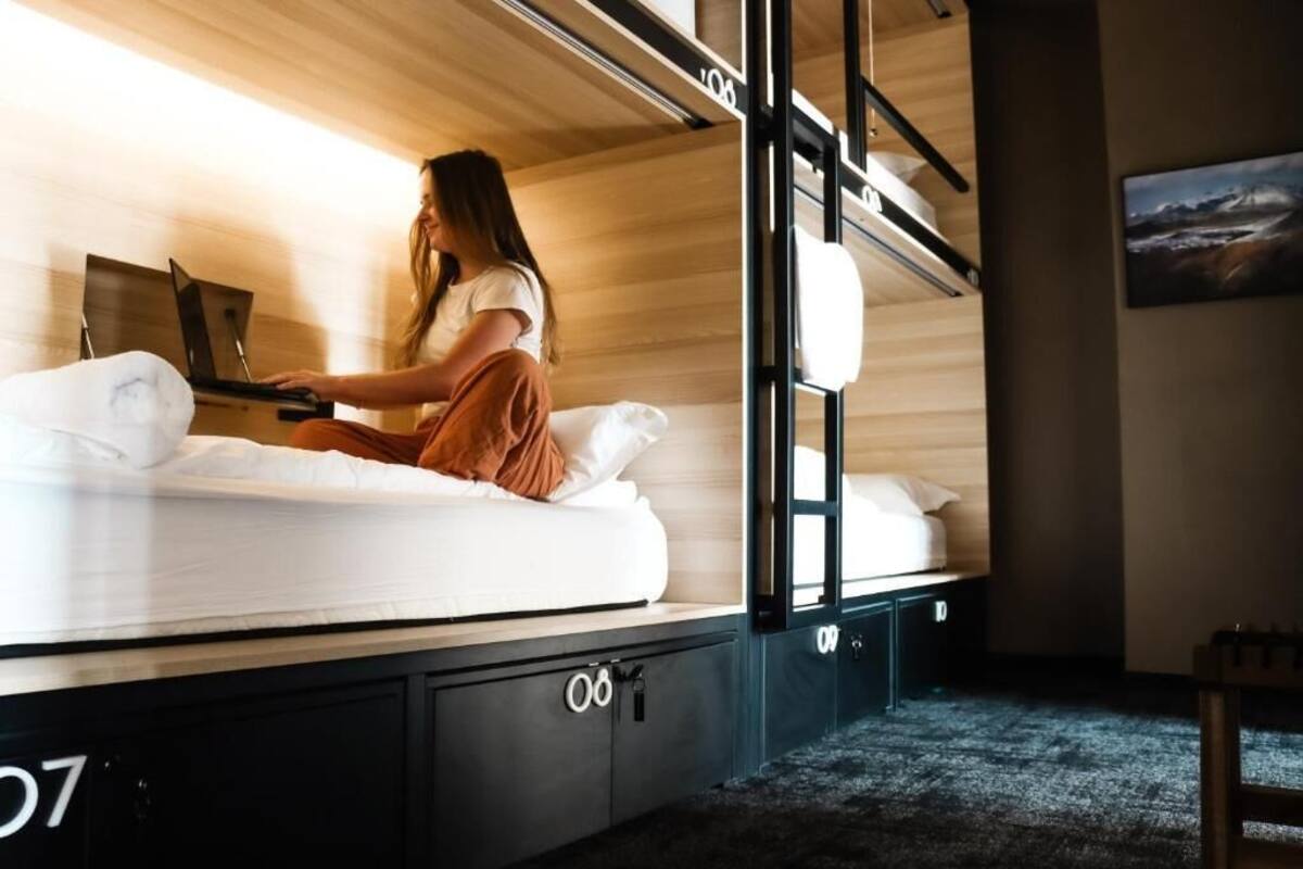 A bunk bed room with a laptop on the lower bunk, a bed with white bedding, and a small desk with a chair.