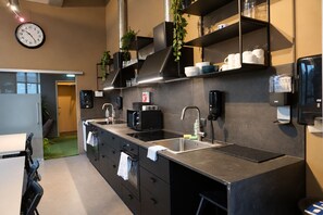 Una cocina moderna con encimera de acero inoxidable, microondas, fregadero y un reloj en la pared.