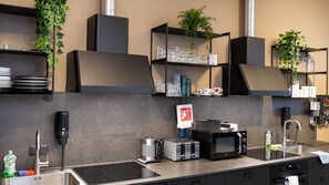 A modern kitchen with a built-in stove, microwave, and sink. There are shelves with glassware and a sign indicating a grand opening. - Nordic Hostel (Reykjavik)