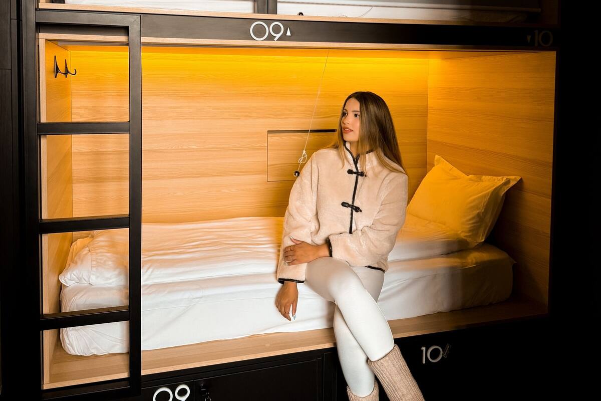A bunk bed with a wooden headboard and a lower bed with white bedding. There is a ladder on the left side of the bunk bed.