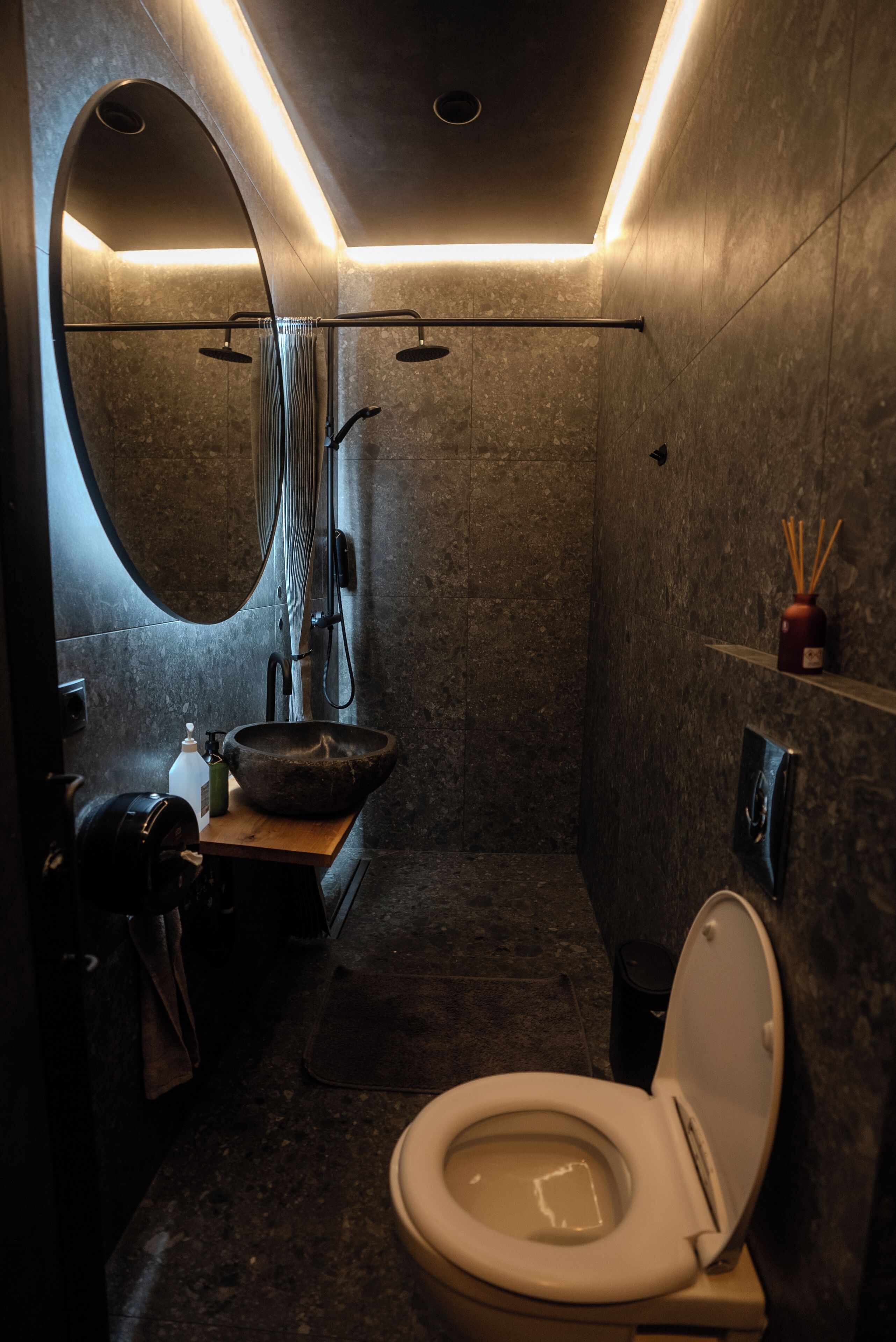 Un baño moderno con un espejo grande, un lavamanos redondo, un inodoro y una zona de ducha.