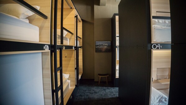 Habitación de hotel con literas, un taburete pequeño y un cuadro en la pared.