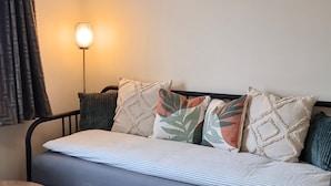Een bed met een gestreept dekbedovertrek, een hoofdbord en meerdere kussens, waaronder een met een bladmotief.