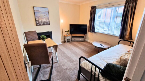 Ein kleines Hotelzimmer mit Bett, Schreibtisch, Stuhl, Fernseher und einem fensterbepflanzten Fenster.