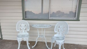 Deux chaises en métal blanc et une petite table ronde sur une terrasse en béton.