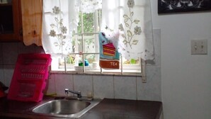 A kitchen with a wooden countertop, a stainless steel sink, a window with floral curtains, a tea bag holder, and a decorative sign on the wall. - Horse Shoe Villas A family friendly 2 bedroom villa near to it all  (Port Antonio)