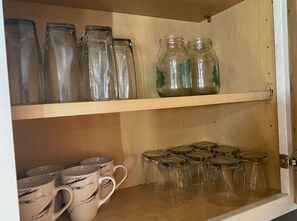 Una estantería de madera con frascos de vidrio y tazas.