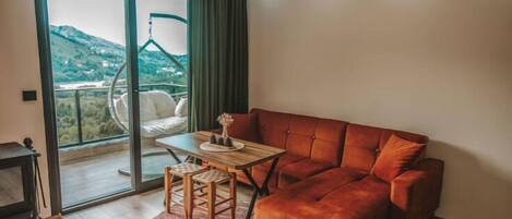 A modern living room with a sofa, a small table, and a hanging chair by a large window.
