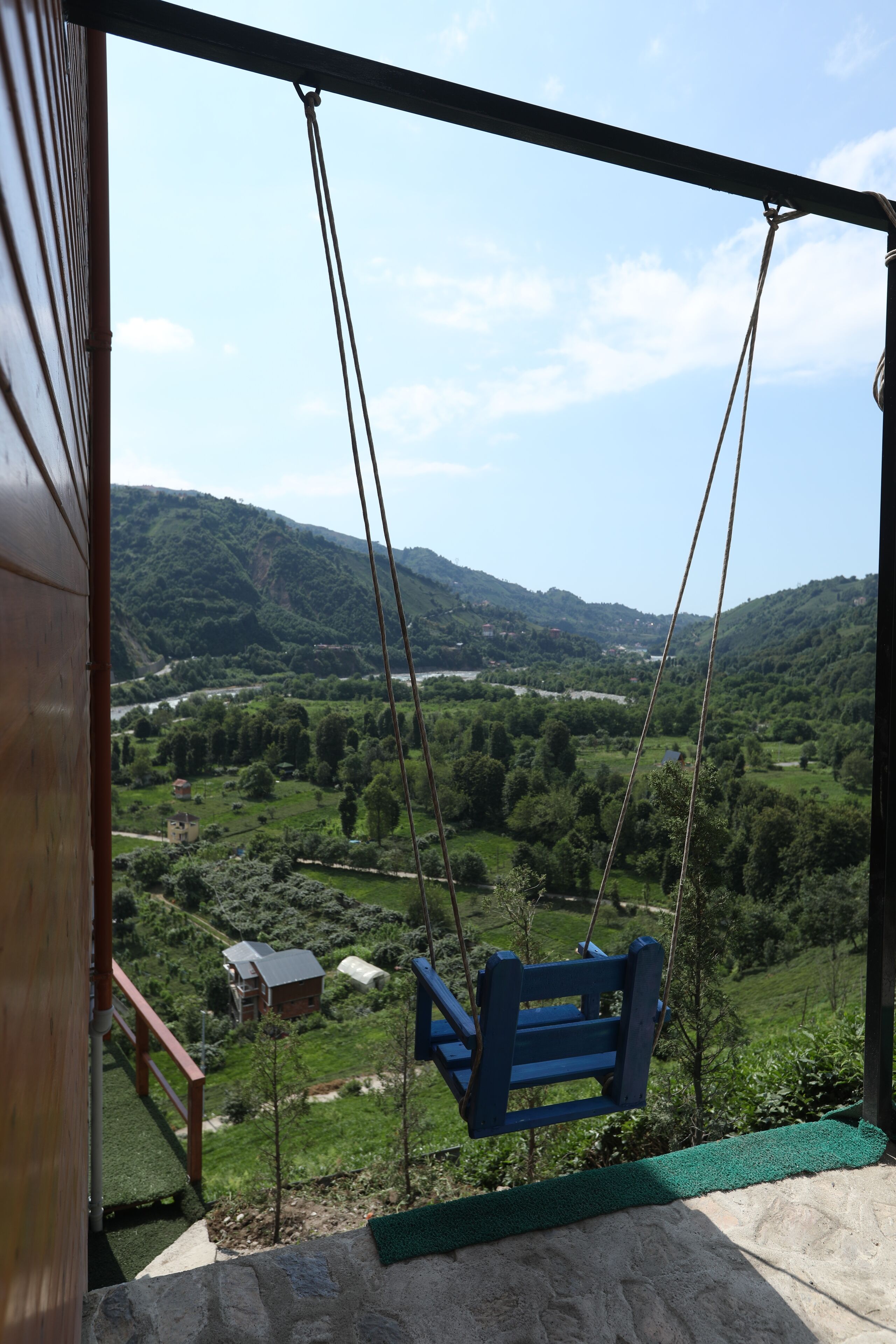 A swing chair overlooking a scenic valley with houses and greenery.