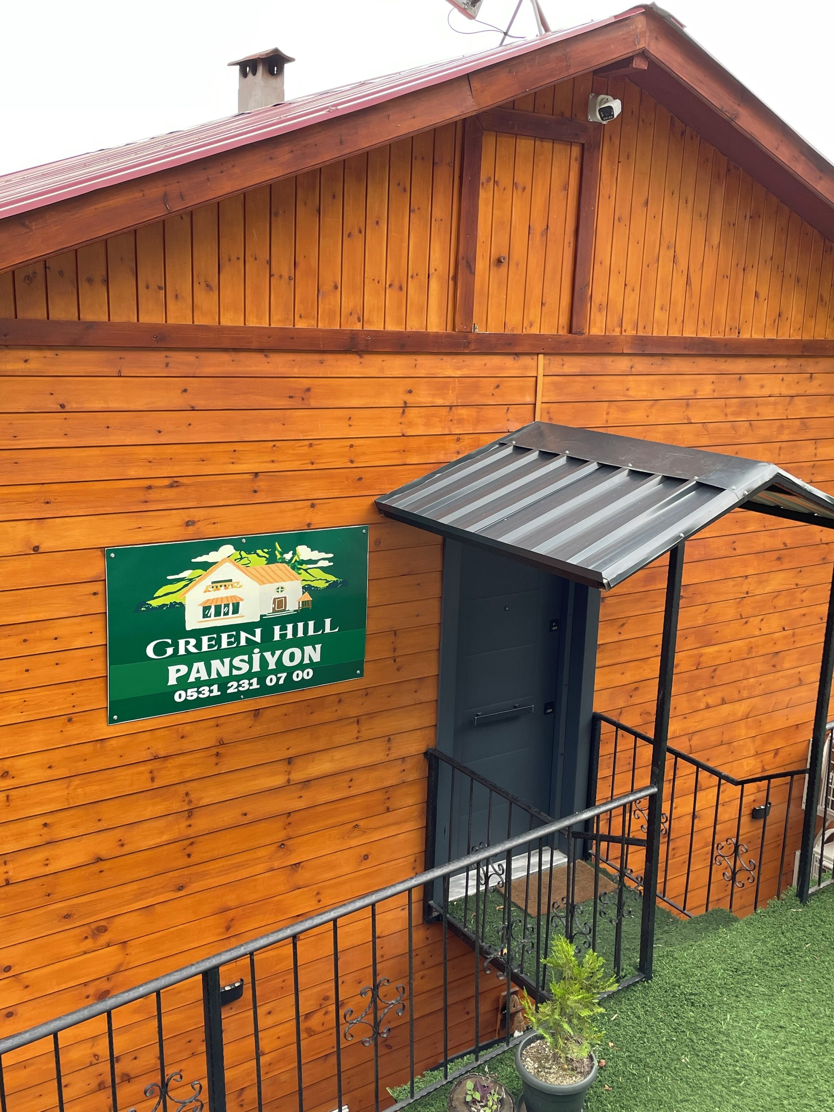 A wooden building with a green sign advertising 'Green Hill Pansiyon' and a small covered entrance.