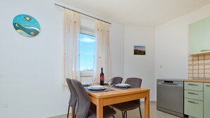 Cocina compacta con lavavajillas, una mesa de comedor lista para dos personas con sillas y una ventana con cortinas.