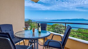 Una mesa redonda con cuatro sillas en un balcón con vistas panorámicas al mar y a las montañas.