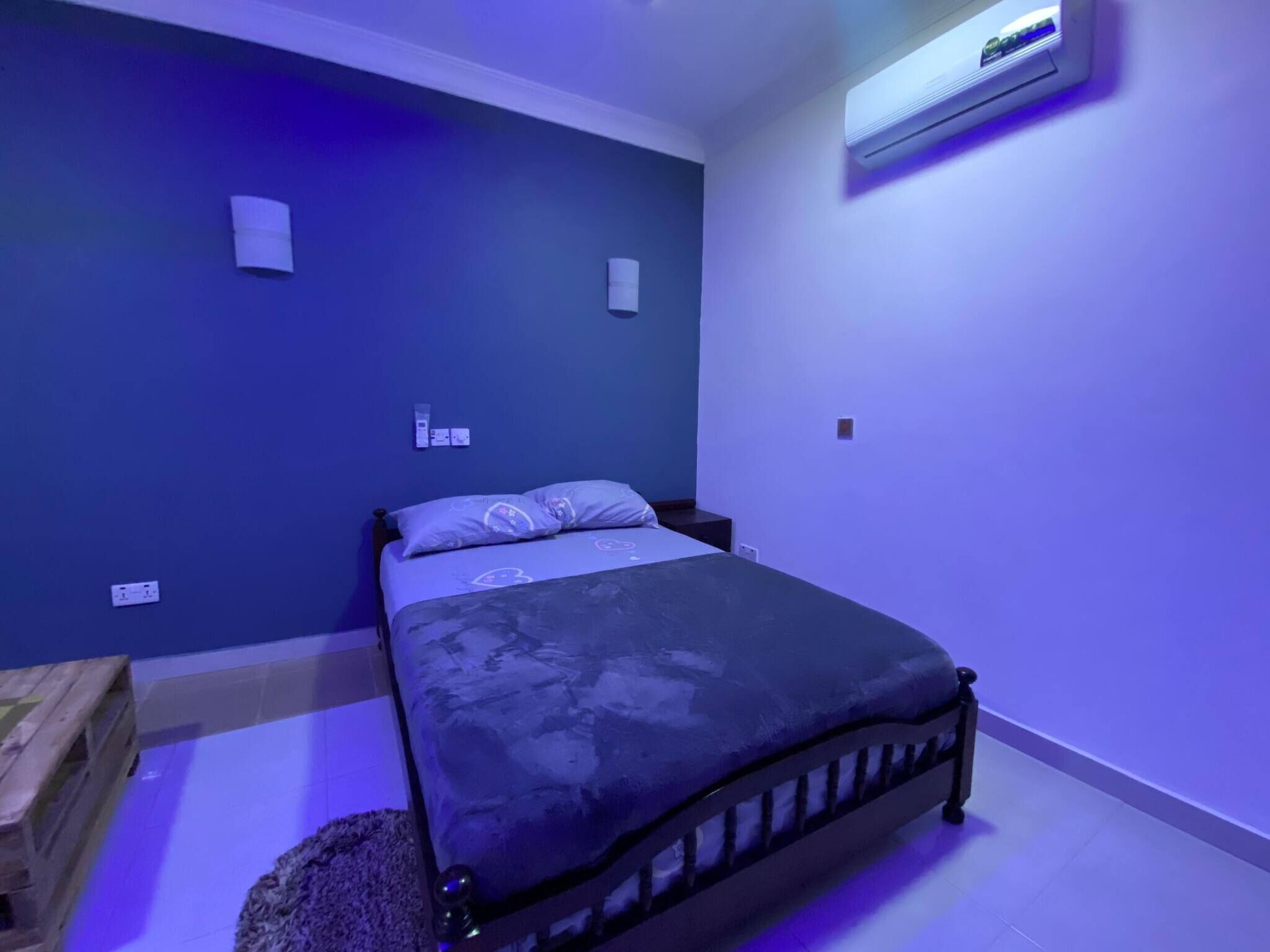 Une chambre à coucher comprenant un lit, une table de chevet en bois, un appareil de climatisation et une prise électrique murale.