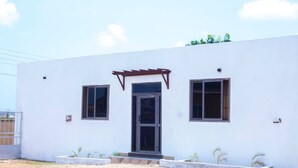 A modern building with a white facade, a central entrance with a glass door, and two windows on either side. - Fully Furnished Studio Apartment (Tema)