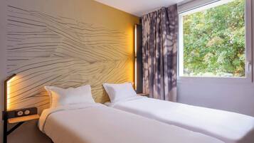 A hotel room with two beds, a modern headboard, a nightstand with a lamp, and a window with curtains.
