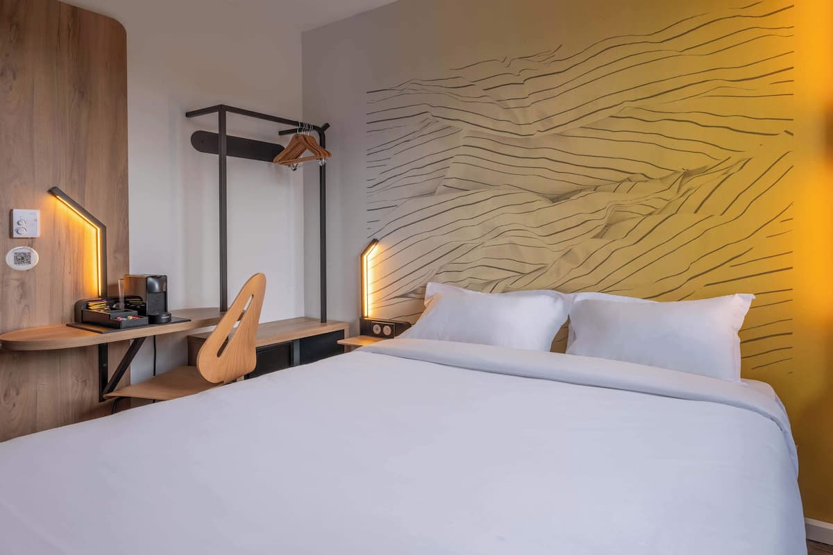 Una habitación de hotel moderna con una cama grande, un escritorio de madera con una silla, un perchero en la pared y un diseño de pared con textura único.