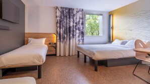 A hotel room with two single beds, a small table, a TV, and a window with curtains.
