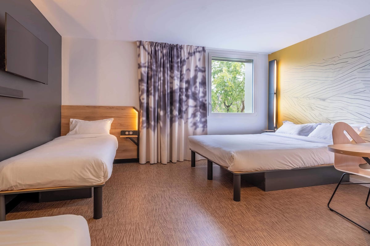 Habitación de hotel con dos camas individuales, una mesita, un televisor y una ventana con cortinas.