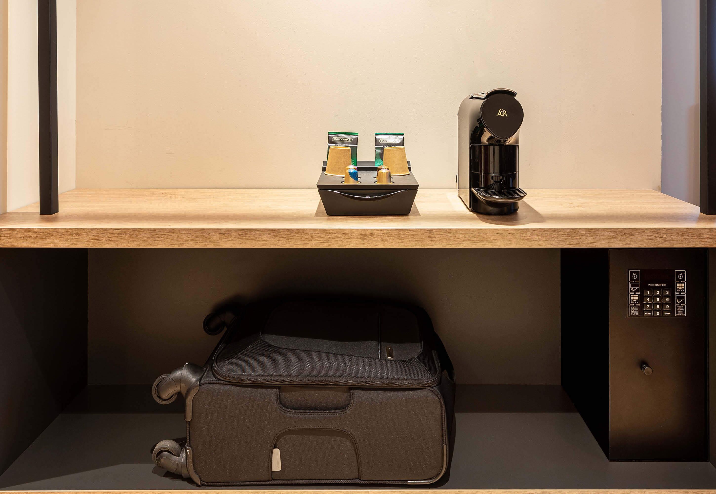 Una estantería con una cafetera, una caja de cápsulas de café y una maleta.