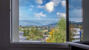 A window view of a town with houses, trees, and mountains in the distance.