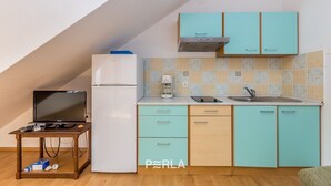 A compact kitchen with teal cabinets, a white refrigerator, a coffee maker, and a small table with electronic devices.