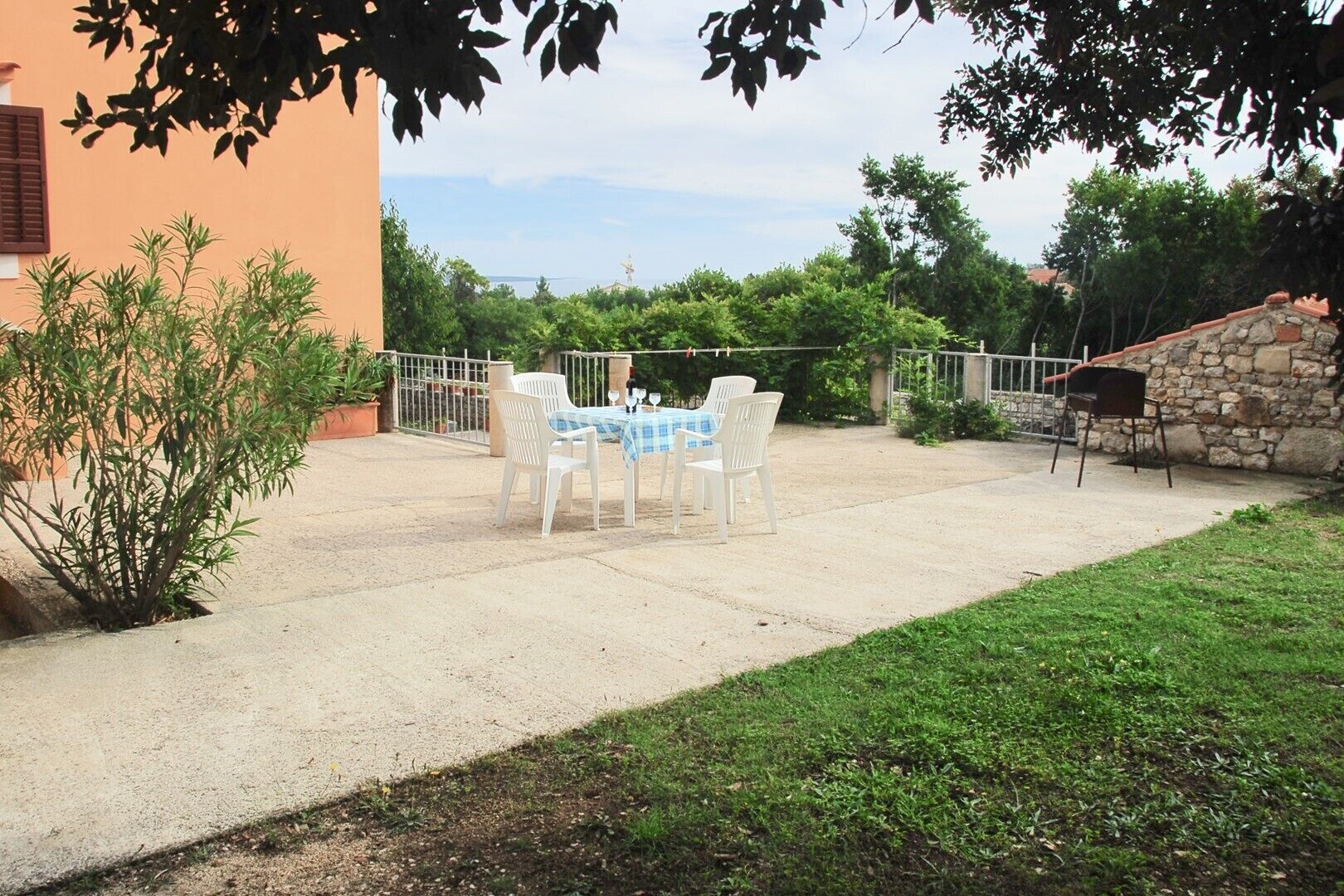 Un patio exterior con una mesa y sillas, rodeado de follaje y un muro de piedra.