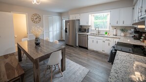 A modern kitchen with white cabinets, stainless steel appliances, and a dining area with a wooden table and chairs. - North Hills Oasis- 5mins from North Hills, Newly Renovated, Two En Suites!  (Raleigh)
