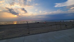 Een strand met een heldere lucht en de zon die ondergaat of opkomt. Er zijn mensen en een bord op het strand.