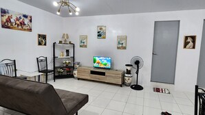 Een woonkamer met een televisie, een ventilator, een bank en een kast met decoratieve spullen.