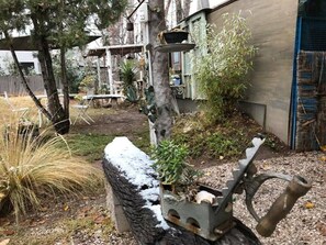 A rustic outdoor area with a stone bench, a metal structure with a plant pot, and a tree.