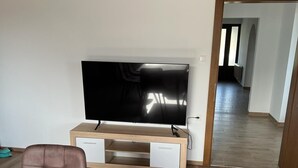 A modern living room with a flat-screen TV on a wooden stand, a brown leather sofa, and a wooden dining table.
