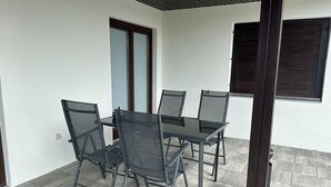 A patio with a table and chairs, a window with blinds, and a door with a window.