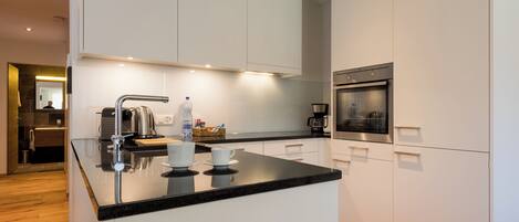 A modern kitchen with white cabinetry, a black countertop, and stainless steel appliances including a coffee maker and oven.