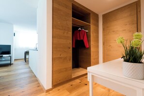 A modern room with wooden flooring, a white table, a potted plant, and a wooden wardrobe with a red garment hanging. - Montela Apartment-Hotel & Resort  (Saas Grund)