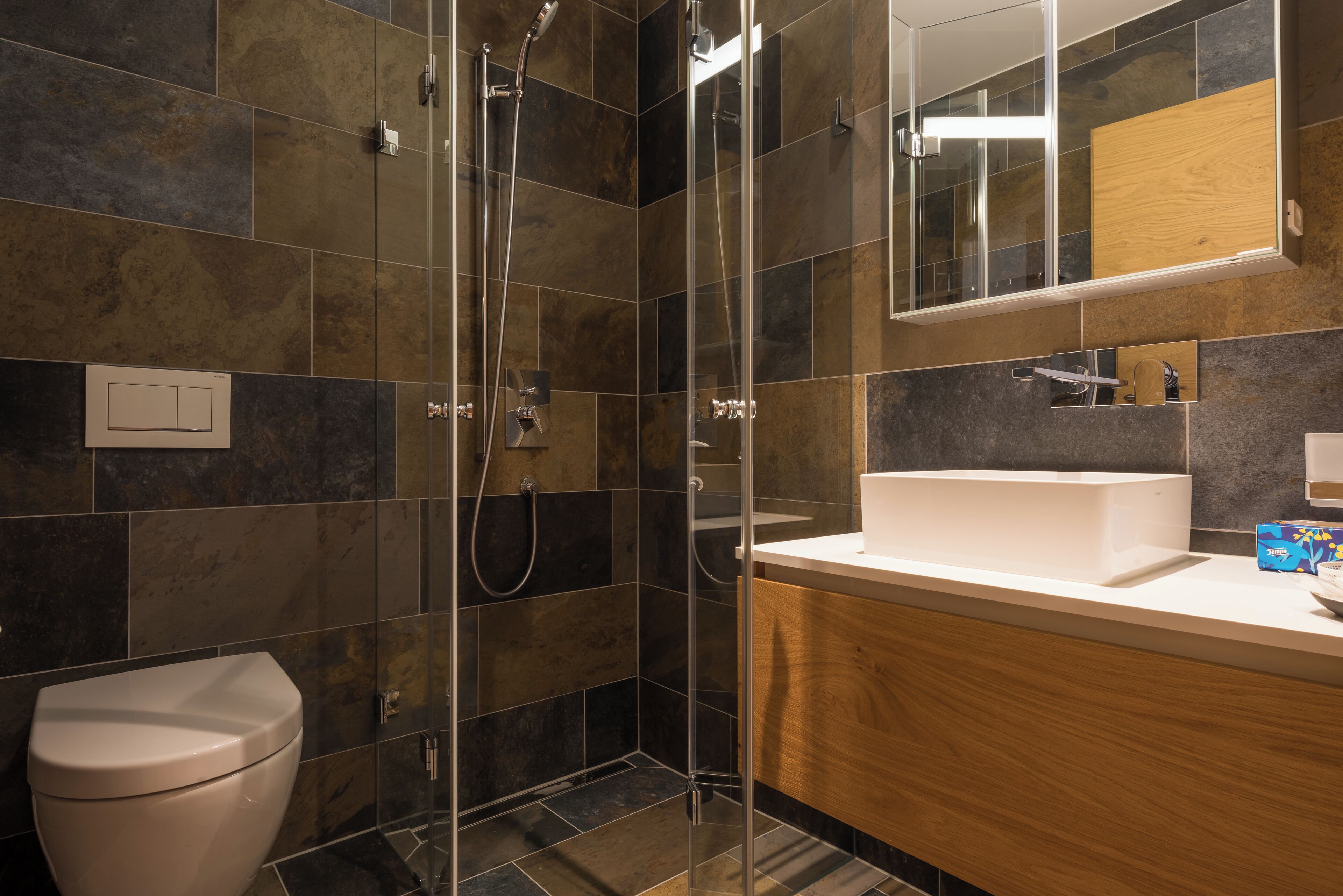 A modern bathroom with a glass-enclosed shower, a white toilet, and a wooden vanity with a sink.
