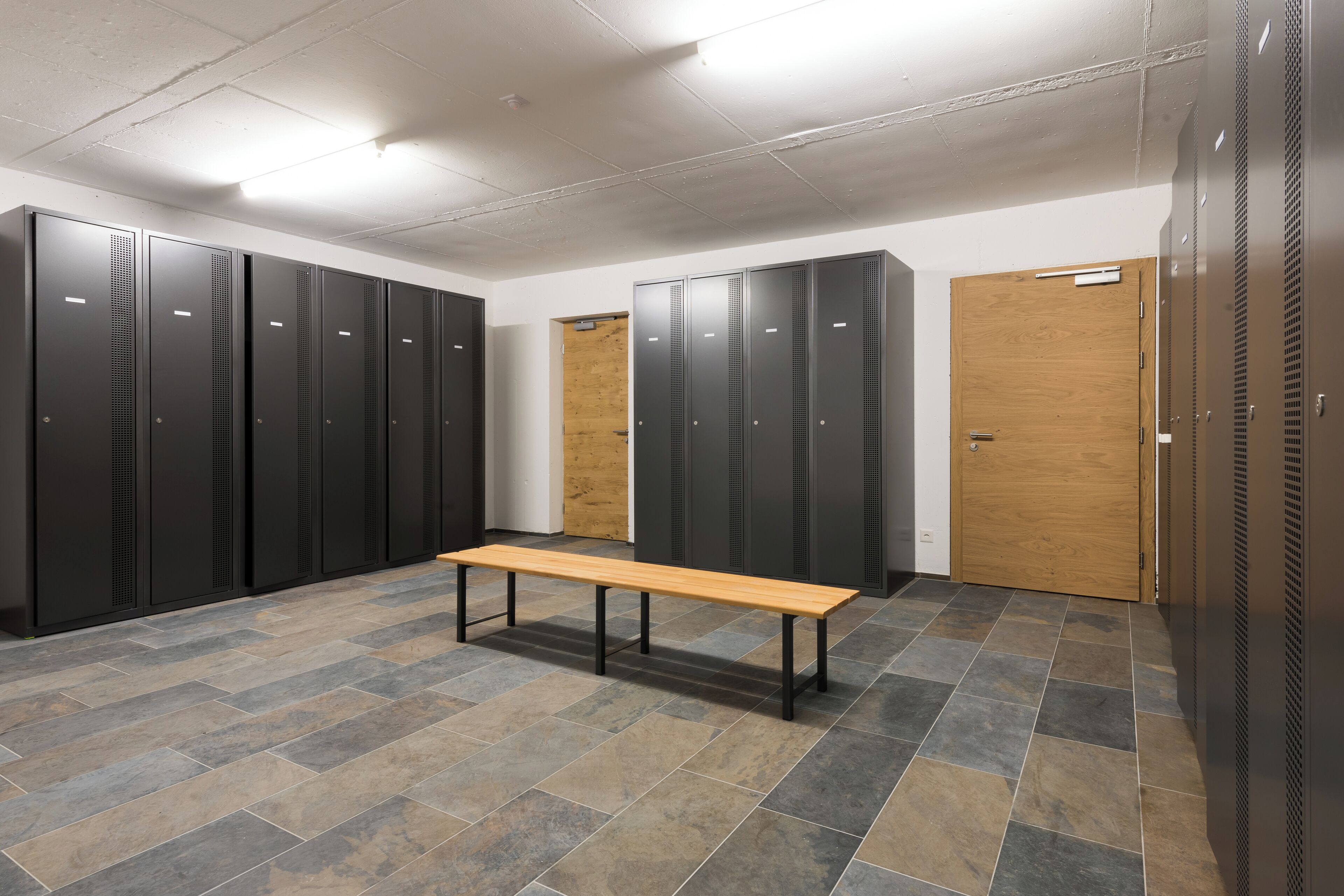 A locker room with multiple lockers, a wooden bench, and a wooden door.