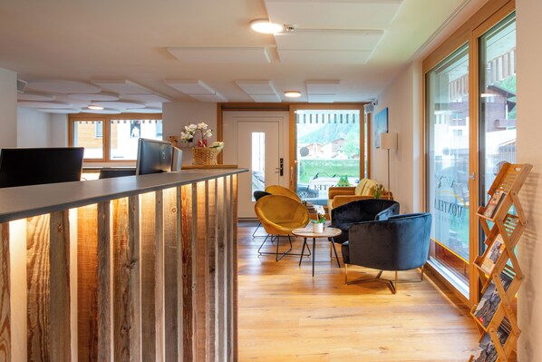 Un hall d’hôtel moderne agrémenté d’éléments en bois, avec un comptoir d’accueil, des sièges confortables et de grandes fenêtres offrant une vue sur l’extérieur.