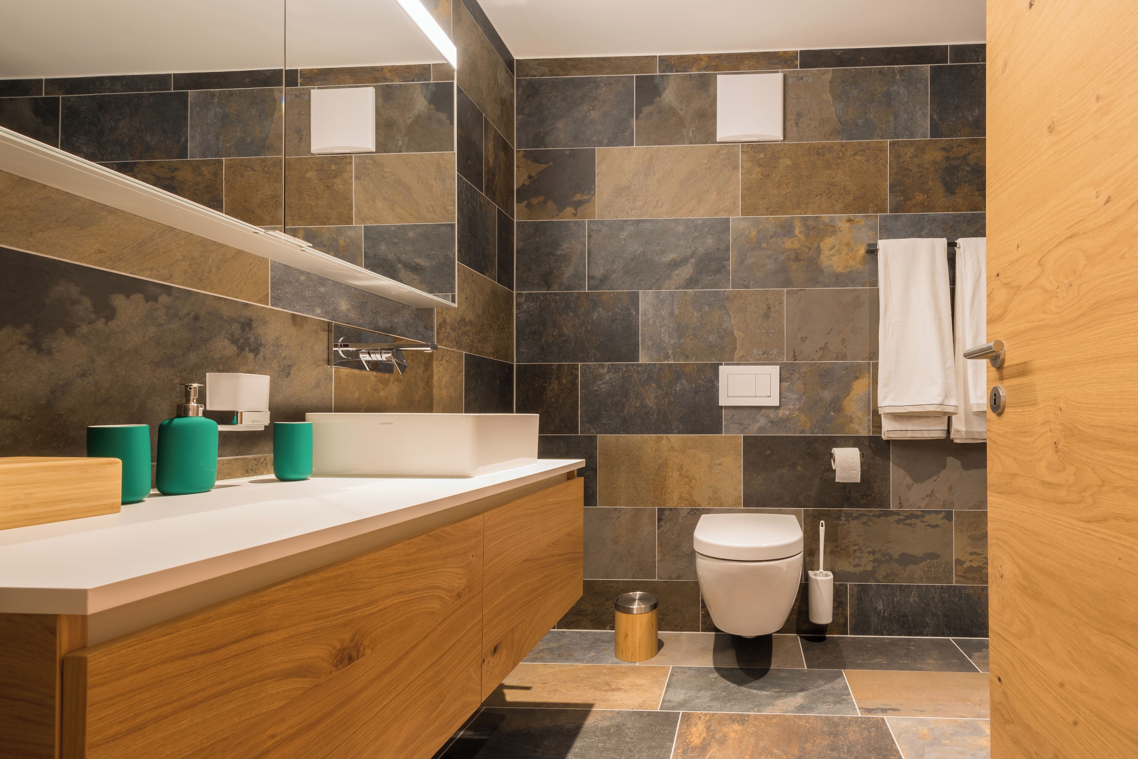 Ein modernes Badezimmer mit einem Holzbadezimmerhocker, einem weißen Waschbecken und einem großen Spiegel.