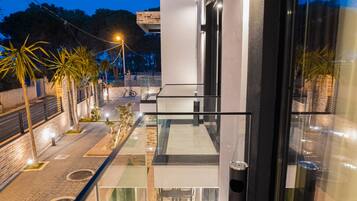 Un edificio moderno con balcón de vidrio, sección de ladrillo y un paseo empedrado bordeado de palmeras.