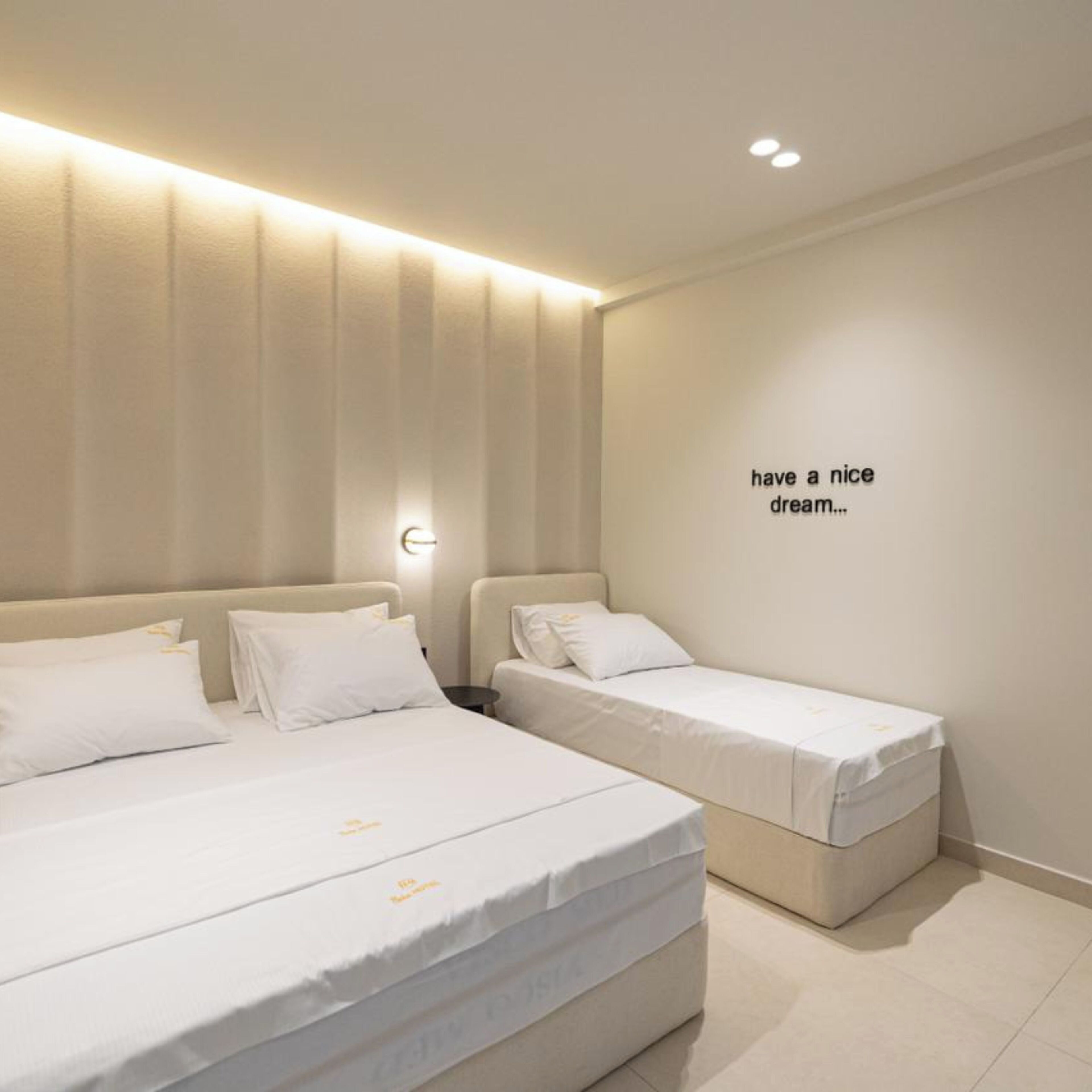 A modern hotel room with a large bed, a smaller bed, and a wall-mounted light fixture.