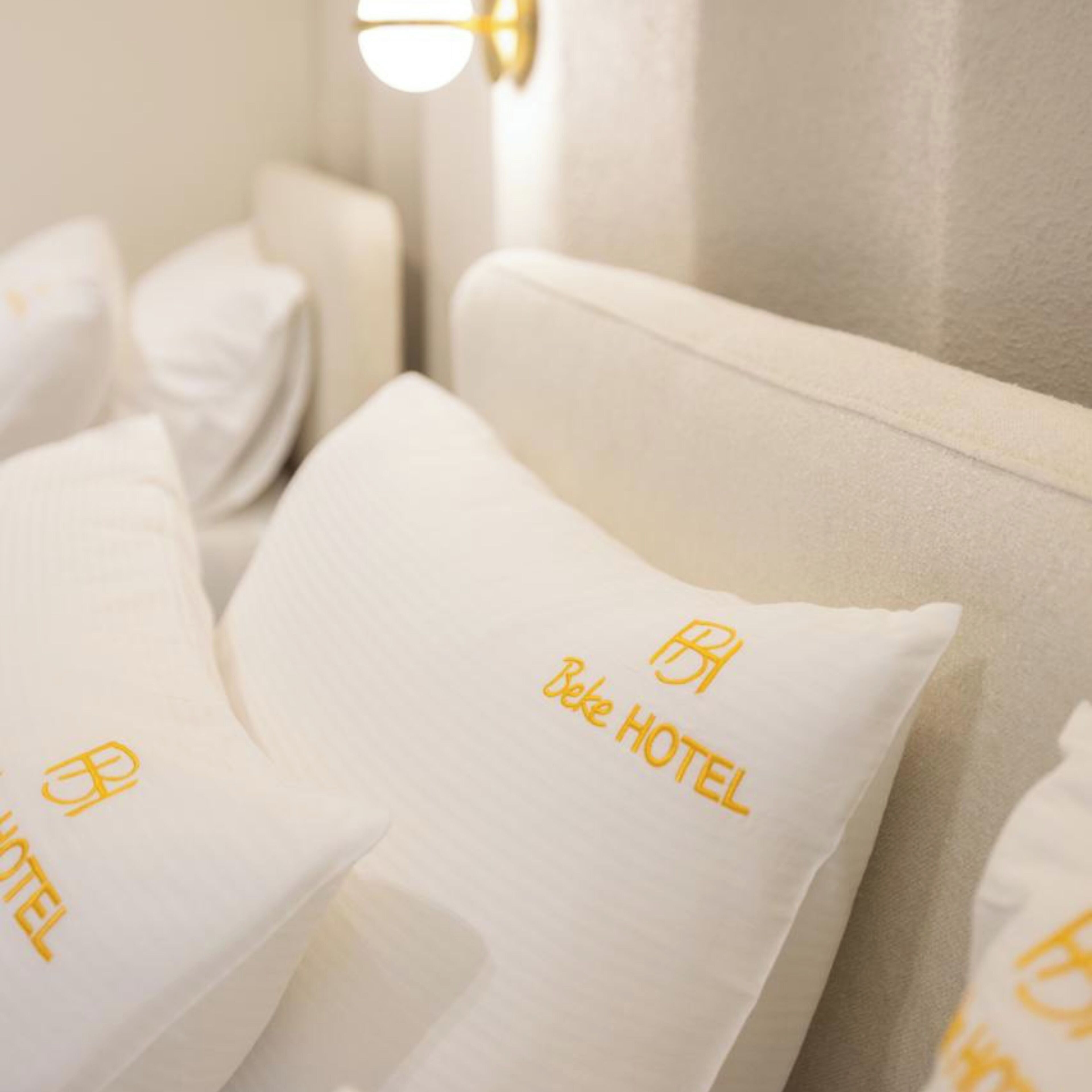 Een hotelbed met kussens waarop de naam en het logo van het hotel geborduurd staan.