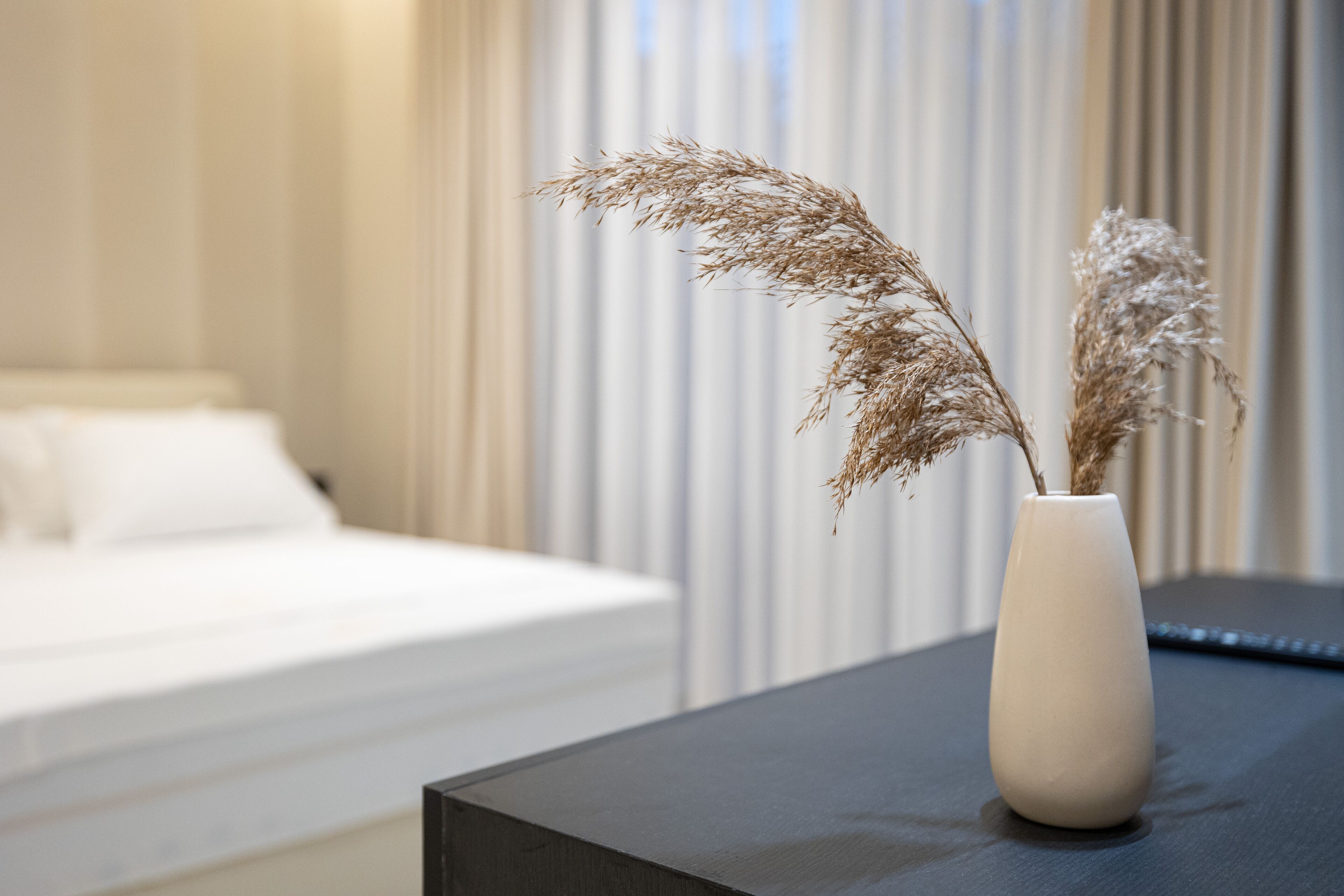 A white vase with dried pampas grass on a dark surface in a hotel room.