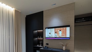 Una habitación de hotel moderna con una televisión de pantalla plana montada en la pared, una mesita de café, una mesita de noche y un ventanal grande con cortinas.